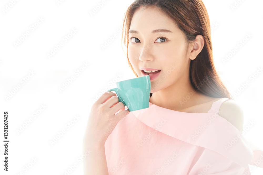 A beautiful young woman is drinking coffee from a blue cup, standing in front of a sunlit window with her back to the sunlight A beautiful young woman is drinking coffee from a blue cup, standing in front of a sunlit window with her back to the sunlight