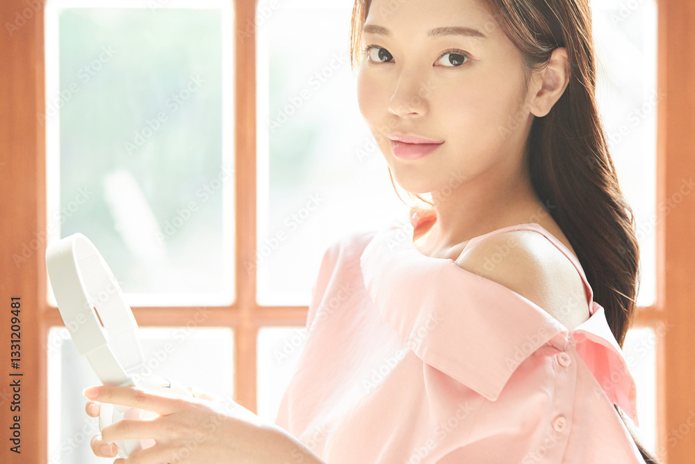A young and beautiful woman is enjoying music with headphones on, standing in front of a window filled with plenty of sunlight. A young and beautiful woman is enjoying music with headphones on, standing in front of a window filled with plenty of sunlight.