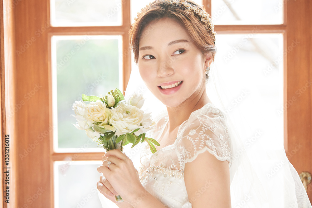 During the wedding ceremony, a young and beautiful bride in a wedding dress stands by a sunlit window. She is holding a bouquet and smiling beautifully amidst swirling flower petals. During the wedding ceremony, a young and beautiful bride in a wedding dress stands by a sunlit window. She is holding a bouquet and smiling beautifully amidst swirling flower petals.