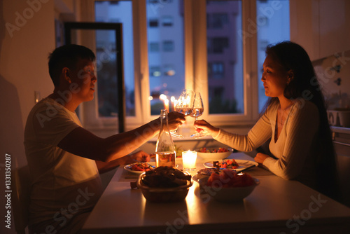 Valokuva Couple toasting with wine glasses, enjoying romantic candlelit dinner at home