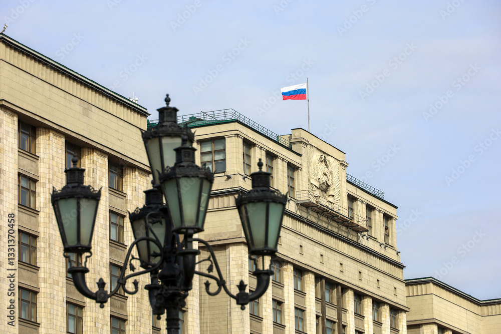 Parliament building with Russian flag in Moscow. The State Duma facade, view through the street lantern Parliament building with Russian flag in Moscow. The State Duma facade, view through the street lantern