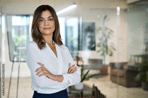 Free Download Smiling middle aged mature professional business woman, female company CEO owner manager executive wearing white blouse standing arms crossed in office at work, looking at camera, portrait. - GFXLoad