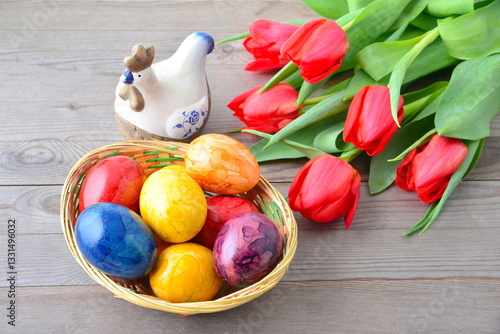 Quadro em tela Easter eggs in basket, red tulips and ceramic hun on wooden background
