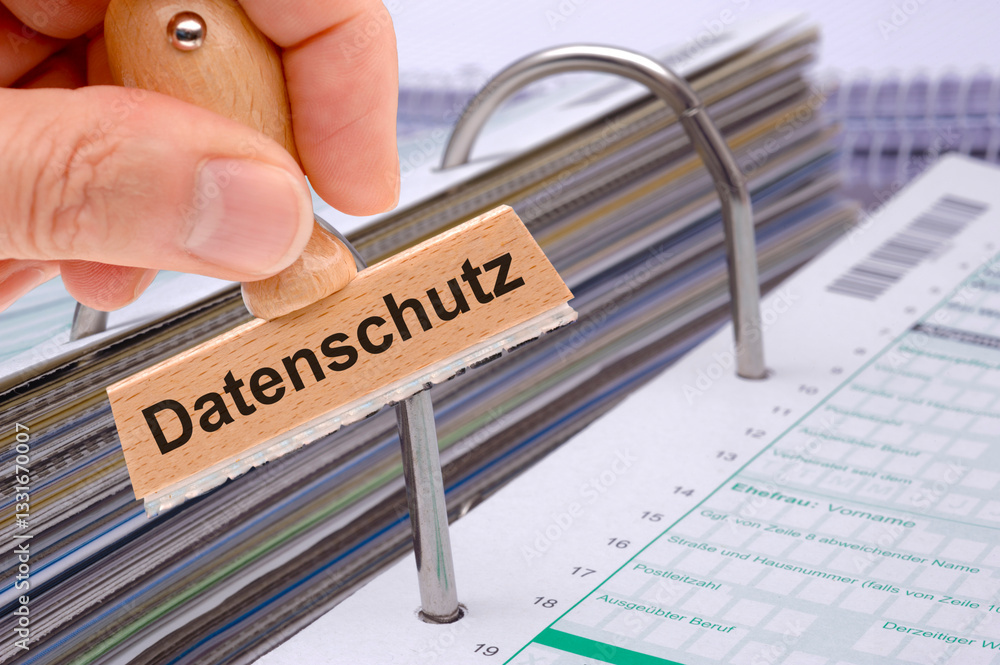 Eine Hand hält einen Holzstempel mit der Aufschrift Datenschutz über einen Aktenordner mit Formularen und Dokumenten - FOTOMONTAGE