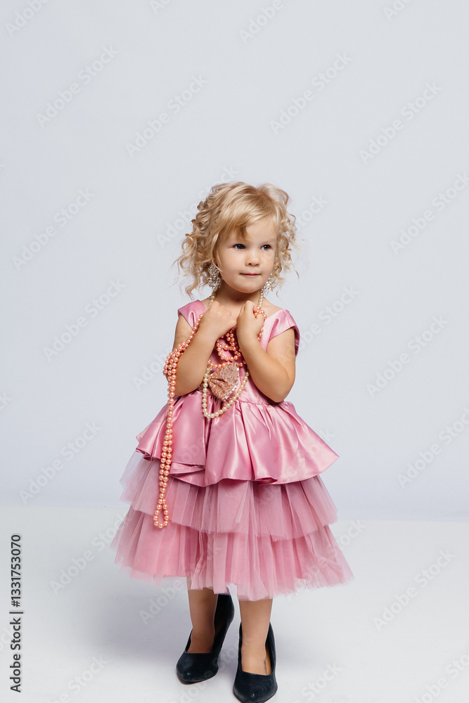 Little girl in a pink dress with pearls posing gracefully against a neutral background Little girl in a pink dress with pearls posing gracefully against a neutral background