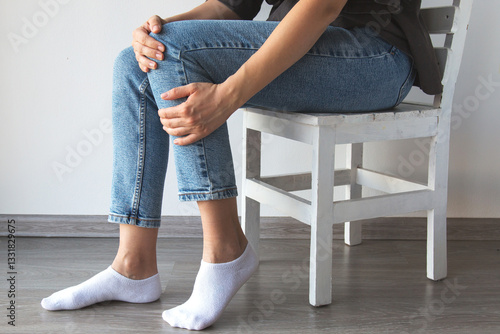 Vászonkép A person sitting on a wooden chair, holding their knee as if experiencing pain o