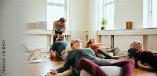 Restorative yoga teacher working with students. All the students lie on the floor on a mat with a pillow over their eyes.