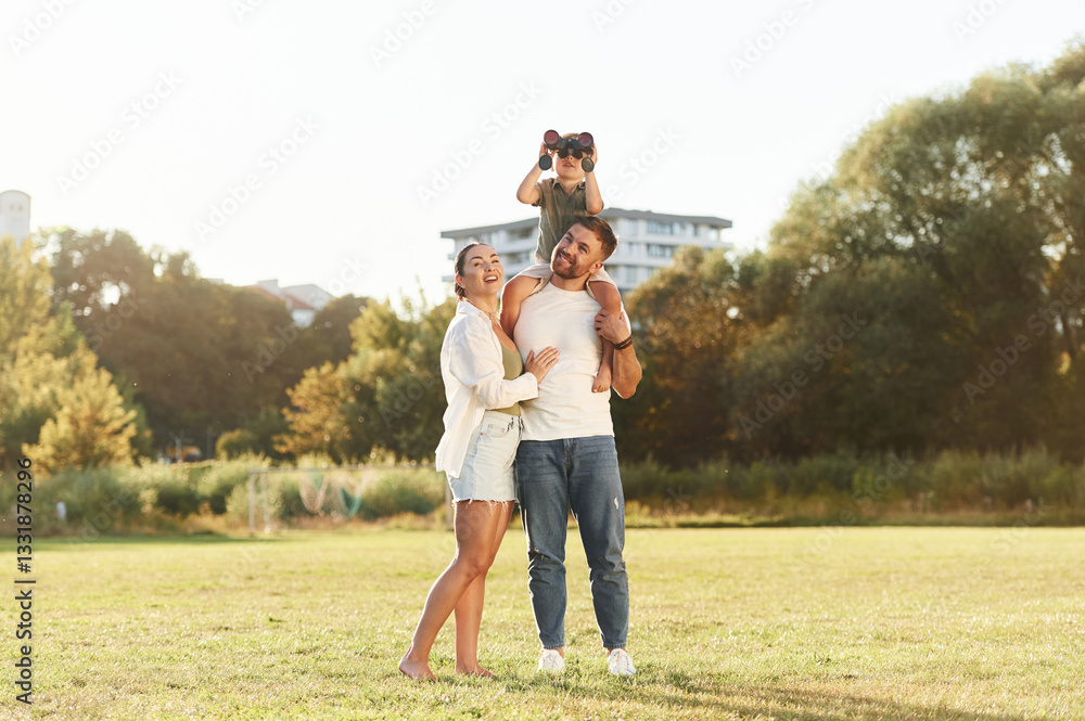 Obraz premium Looking far away with binocular. Mother and father are with son outdoors on the field