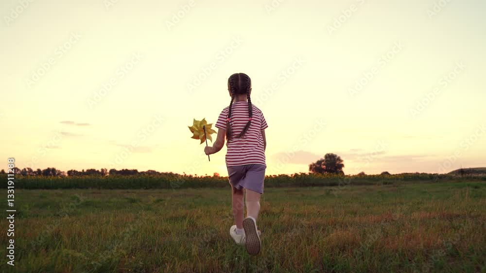 Little girl holds windmill toy having fun in field at sunset time. Preschooler girl enjoys game with rotating windmill toy in evening park. Cute little girl raises windmill running in rural meadow Little girl holds windmill toy having fun in field at sunset time. Preschooler girl enjoys game with rotating windmill toy in evening park. Cute little girl raises windmill running in rural meadow