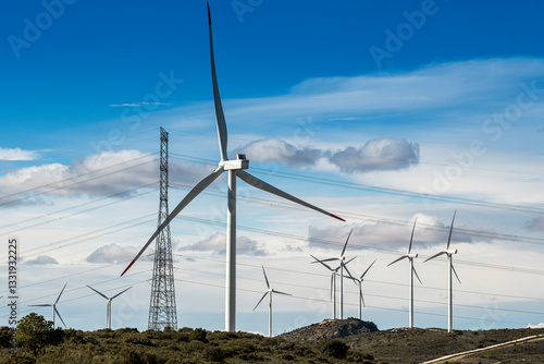 Wind turbines spinning in a renewable energy farm, with electrical towers in the background, highlighting energy infrastructure.