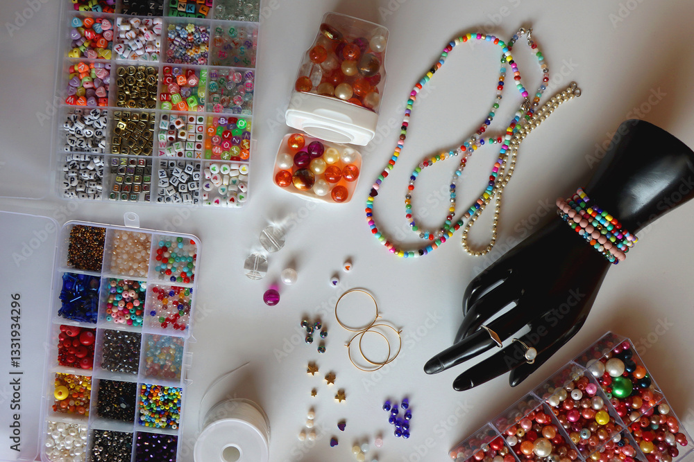 Hand figurine, colorful friendship bracelets, necklaces, various beads and DIY supplies on the table. Making jewelry at home. Flat lay.