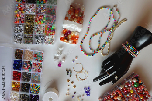 Hand figurine, colorful friendship bracelets, necklaces, various beads and DIY supplies on the table. Making jewelry at home. Flat lay.