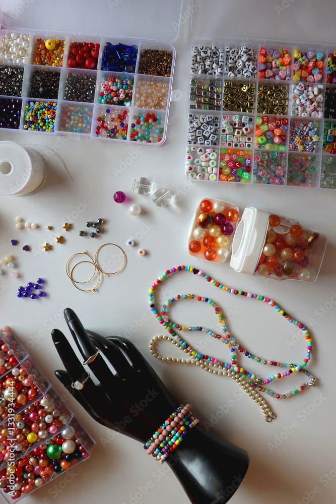 Hand figurine, colorful friendship bracelets, necklaces, various beads and DIY supplies on the table. Making jewelry at home. Flat lay.