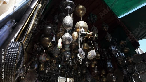 Collection of ornate Moroccan metal lanterns and decorative hanging ornaments, featuring intricate patterns and warm golden tones in a market setting