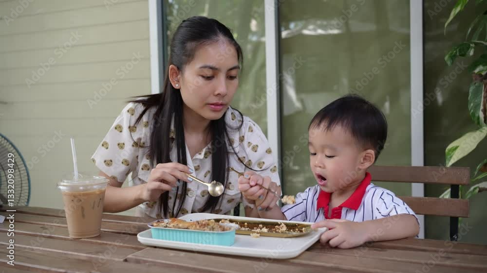 Young mother and cheerful toddler enjoy eating a banana cake on wooden table in the garden Young mother and cheerful toddler enjoy eating a banana cake on wooden table in the garden