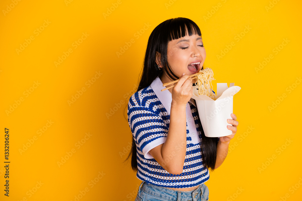 Young woman enjoying noodles from a takeout box against a vibrant yellow background, expressing joy and a carefree lifestyle Young woman enjoying noodles from a takeout box against a vibrant yellow background, expressing joy and a carefree lifestyle