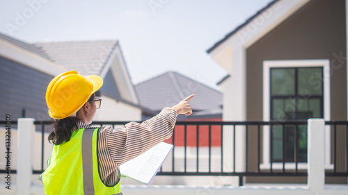 Wallpaper Mural A female engineer inspects the construction site of a housing project, holding a blueprint in her hand and pointing at a house in the background. Torontodigital.ca