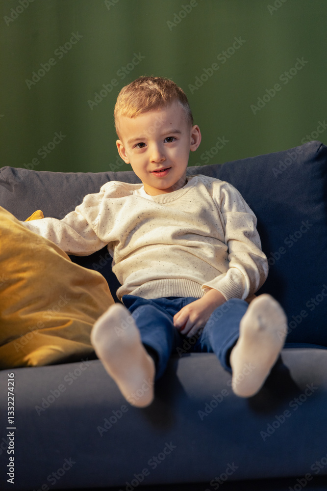 Blond boy relaxing on sofa with white socks and green background Blond boy relaxing on sofa with white socks and green background
