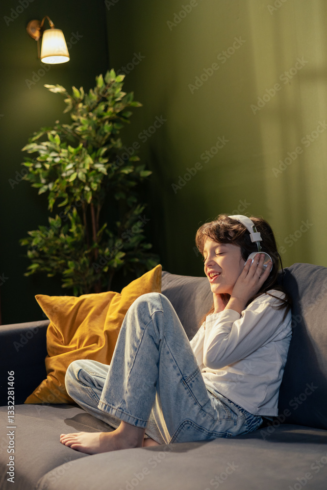 Obraz premium Young girl enjoying music with headphones on sofa at home