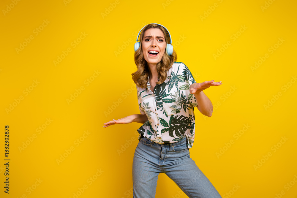 Obraz premium Cheerful young woman wearing headphones and enjoying music on a vibrant yellow background, expressing positive energy.