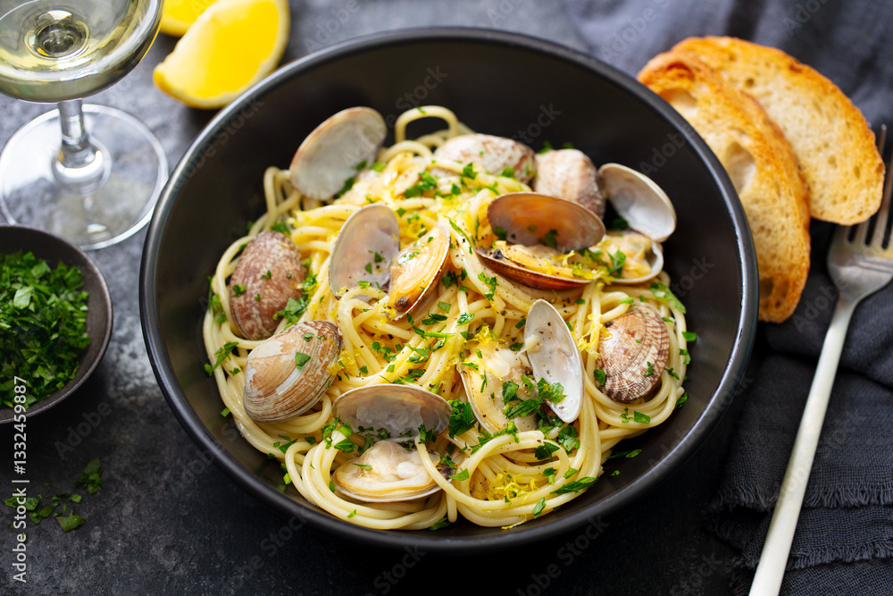 Fototapeta premium Spaghetti alle vongole, seafood pasta with clams in a black bowl and glass of wine. Dark background. Close up.