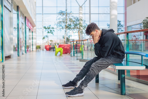 Canvastavla eenager in black hoodie sitting on a bench with head in hands, feeling stressed or overwhelmed, sensory overload, autism, ADHD, bullying, mental health in a bright shopping mall
