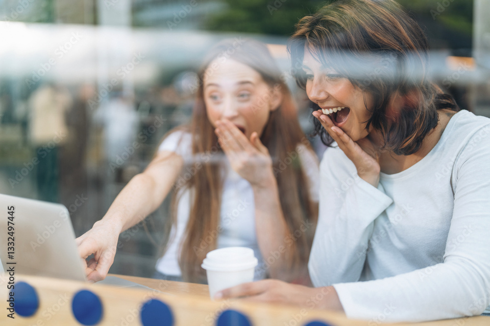 Two friends express excitement while looking at laptop in cafe during sunny afternoon Two friends express excitement while looking at laptop in cafe during sunny afternoon