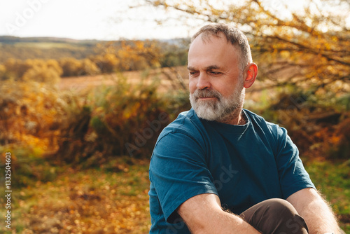 Man relaxing outdoors in autumn landscape, surrounded by colorful foliage and serene countryside views in late afternoon light