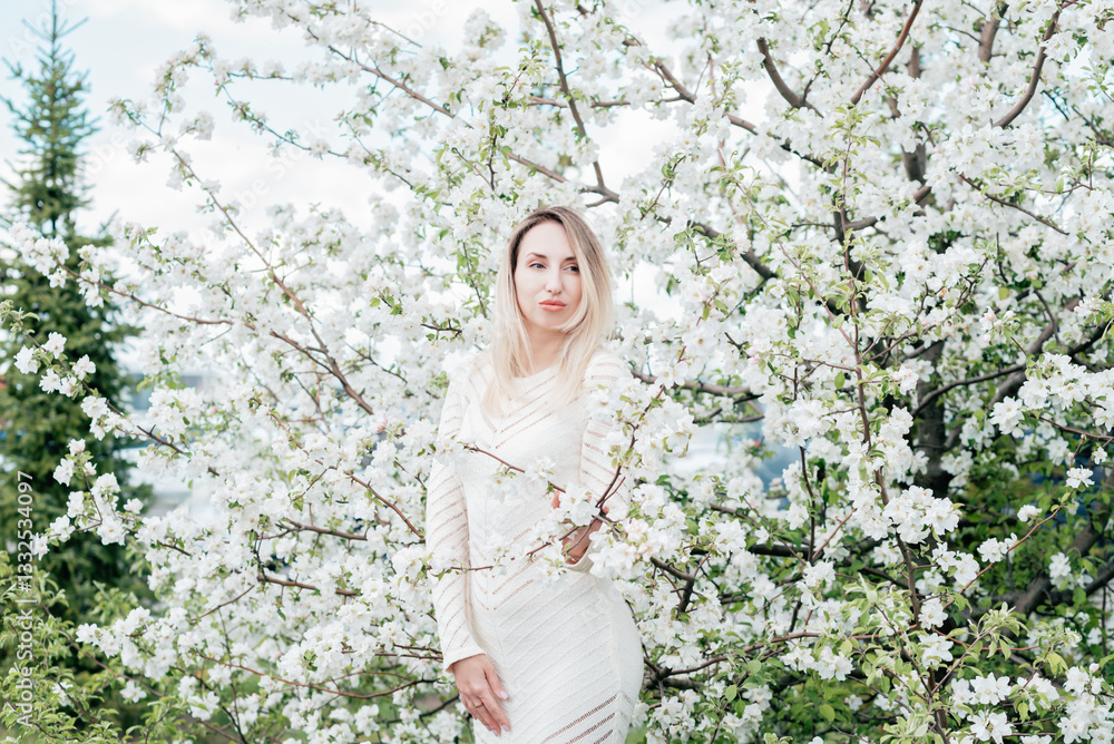Portrait joyful young woman with blonde hair gently holds a cluster of white blossoms near her face while smiling softly. Surrounded by a dreamy backdrop of blooming trees Portrait joyful young woman with blonde hair gently holds a cluster of white blossoms near her face while smiling softly. Surrounded by a dreamy backdrop of blooming trees