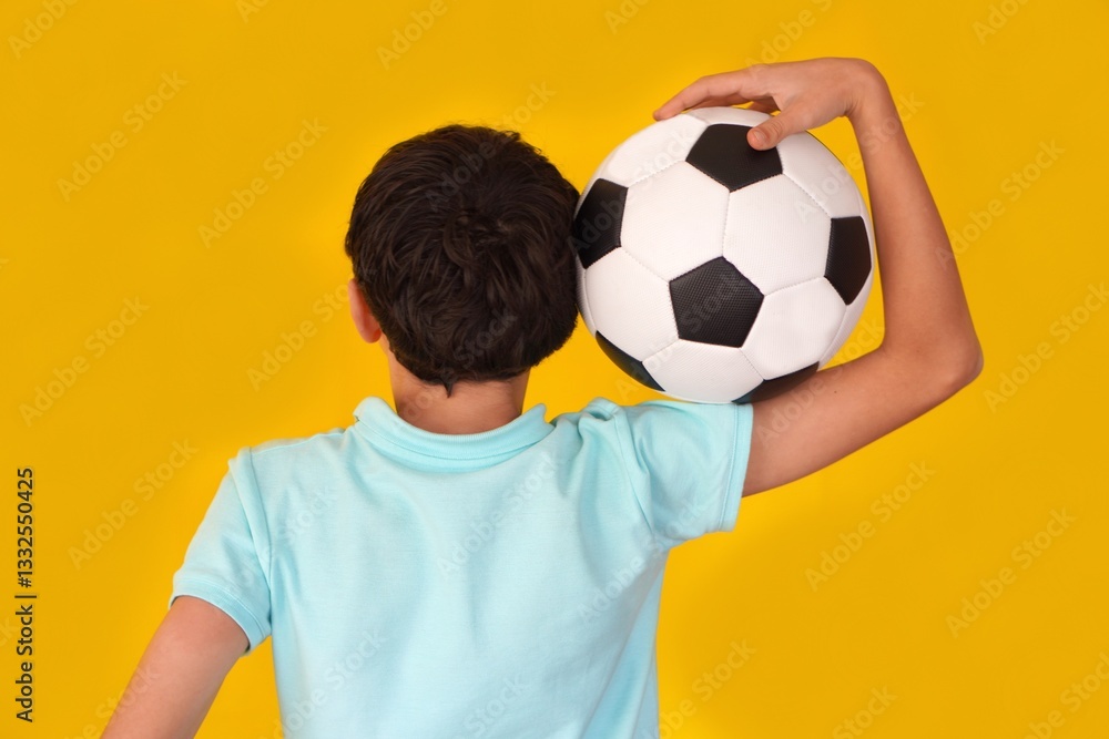 boy on his back with soccer ball on his shoulder. wearing blue polo shirt and yellow background. boy on his back with soccer ball on his shoulder. wearing blue polo shirt and yellow background.