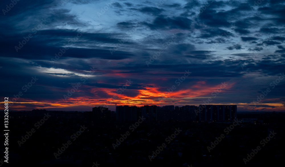 Fototapeta premium City skyline at twilight with dramatic sunset and dark clouds. Urban landscape with high-rise buildings silhouetted against the colorful evening sky.