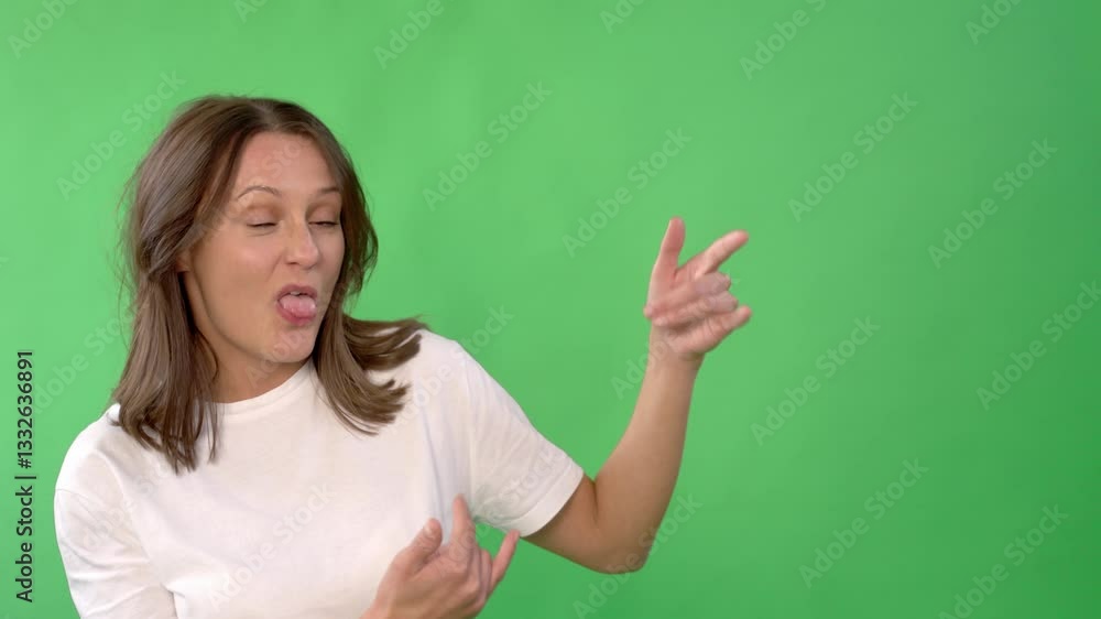 Woman gestures playfully while standing against a green background in a creative studio environment during a casual daytime setting Woman gestures playfully while standing against a green background in a creative studio environment during a casual daytime setting
