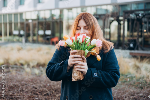 Obraz na płótnie Beautiful young woman with spring tulips flowers bouquet walking at city street. Happy girl posing outdoors. Spring portrait of pretty female on urban background. High quality photo. w salonie