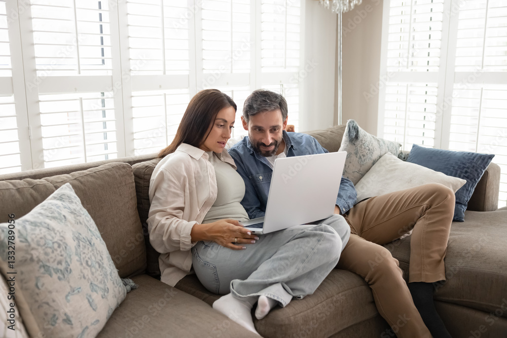 Young middle aged couple in love relaxing on home sofa with laptop computer, watching movie, video content on Internet, using online application for e-shopping, booking Young middle aged couple in love relaxing on home sofa with laptop computer, watching movie, video content on Internet, using online application for e-shopping, booking
