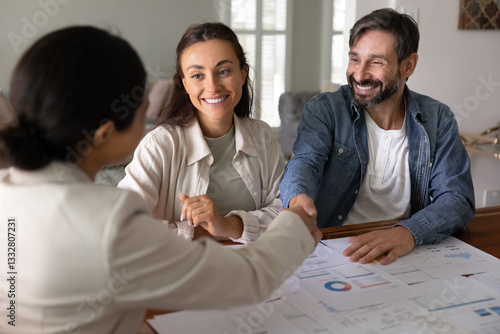 фотографія Happy couple of clients thanking financial adviser for consultation, shaking han