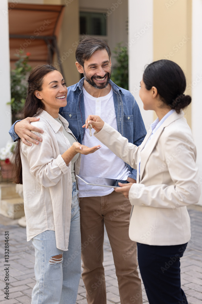 Happy Latin family couple getting new home, taking key from realtor woman, standing outside of new house, receiving accommodation from real estate agent, laughing. Vertical shot Happy Latin family couple getting new home, taking key from realtor woman, standing outside of new house, receiving accommodation from real estate agent, laughing. Vertical shot