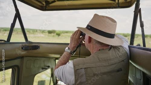 Male explorer or researcher is looking for animals in safari from 4x4 truck. Man using binoculars to watch wild animals in their natural habitat in Africa. Standing inside special game viewer vehicle