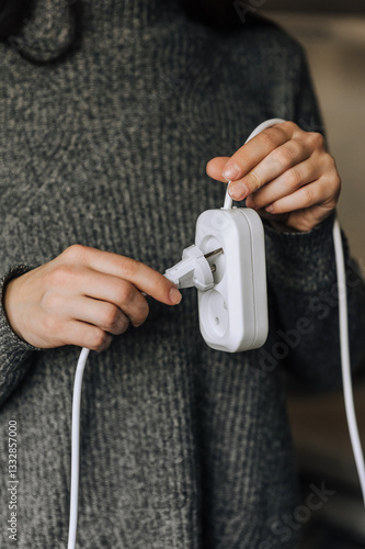 Woman inserting white plug into extension cord socket with her hands to turn on electricity. Photo, technology concept.