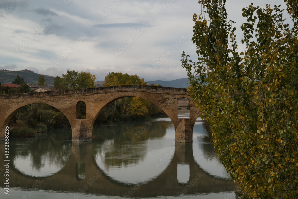 Fototapeta premium Puente de la Reina or Gares Bridge with its reflection in the Arga River, located in Navarra. The iconic Bridge of the Pilgrims of the Camino de Santiago Frances, route that comes from the Fances side