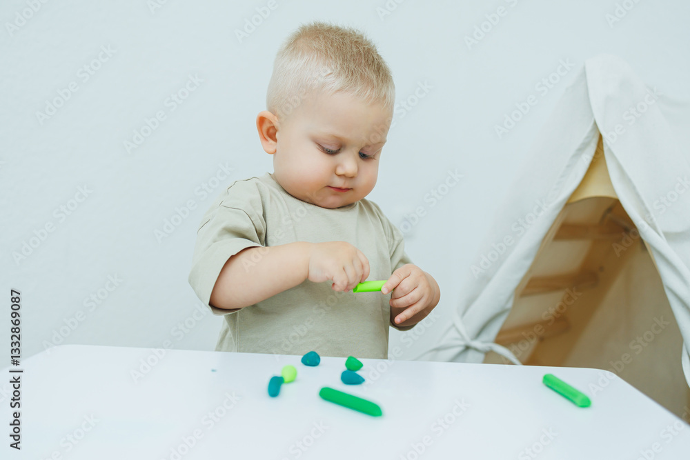 A little one-year-old boy is sculpting plasticine while standing at the table. The child is playing with educational toys. A little one-year-old boy is sculpting plasticine while standing at the table. The child is playing with educational toys.