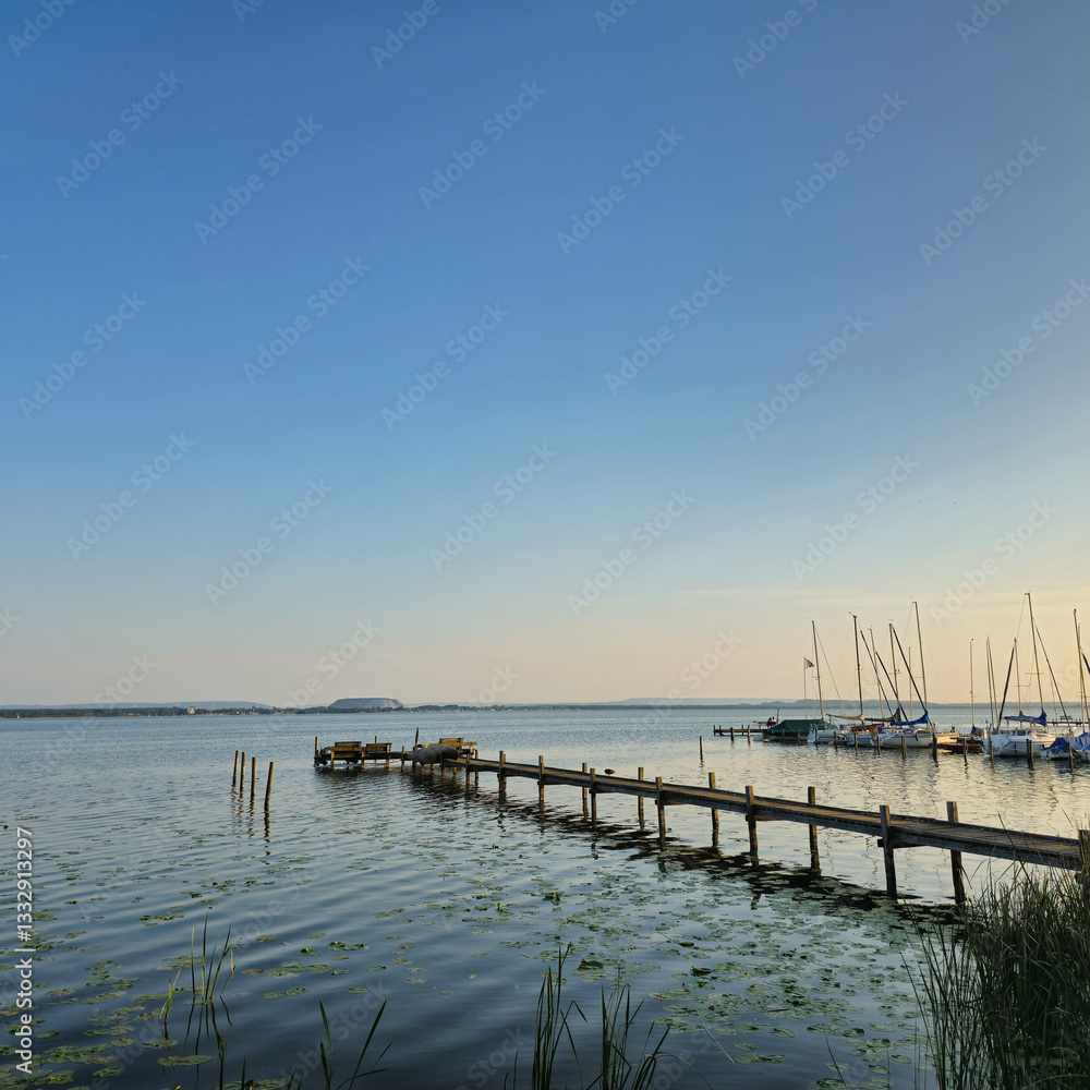 Fototapeta premium A Serene and Beautiful Waterfront View featuring a Pier, Sailboats gently floating at Sunset Steinhuder Meer