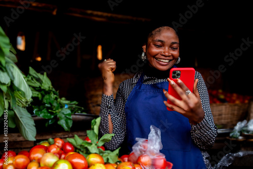 Young African market woman selling tomatoes giving thumbs up holding phone