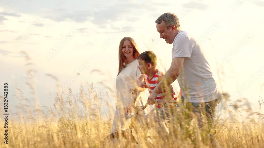 Laughing father pulls bike teaching little son to ride at family weekend at countryside. Parents help boy to ride bicycle at family summer holiday. Caring family with son walks across field at sunset Laughing father pulls bike teaching little son to ride at family weekend at countryside. Parents help boy to ride bicycle at family summer holiday. Caring family with son walks across field at sunset