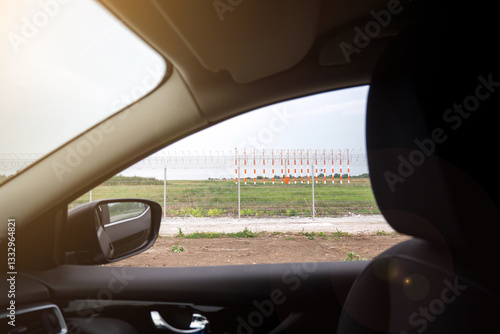 Wallpaper Mural Sunlit view from a car showing a fenced airport area with orange and white runway markers. Ideal for capturing the essence of travel, security, and aviation journeys. Torontodigital.ca