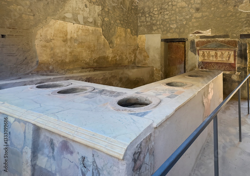 Pompeii, Campania, Italy - July 6, 2024: Ancient Roman City ruins at Via Dell'Abbondanza 8, street, what used to be a fast food business. Artwork in back