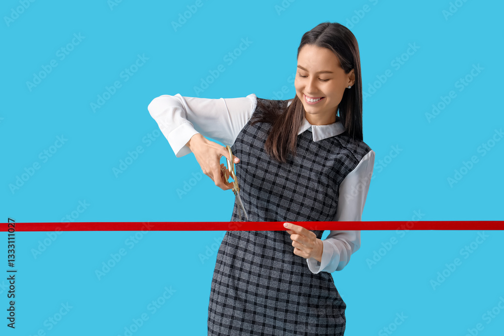Happy young businesswoman cutting red ribbon on blue background Happy young businesswoman cutting red ribbon on blue background