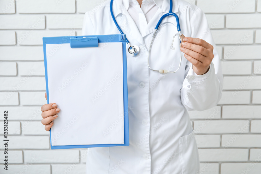 Female doctor with hearing aid and blank clipboard near white brick wall Female doctor with hearing aid and blank clipboard near white brick wall