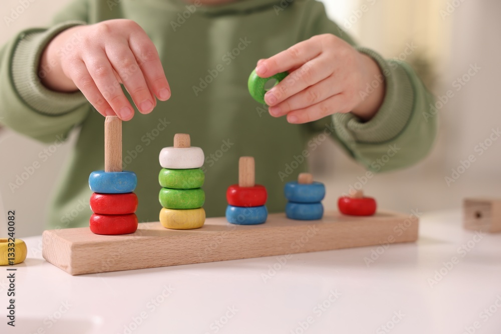 Motor skills development. Little boy playing with stacking toy at white table indoors, closeup Motor skills development. Little boy playing with stacking toy at white table indoors, closeup
