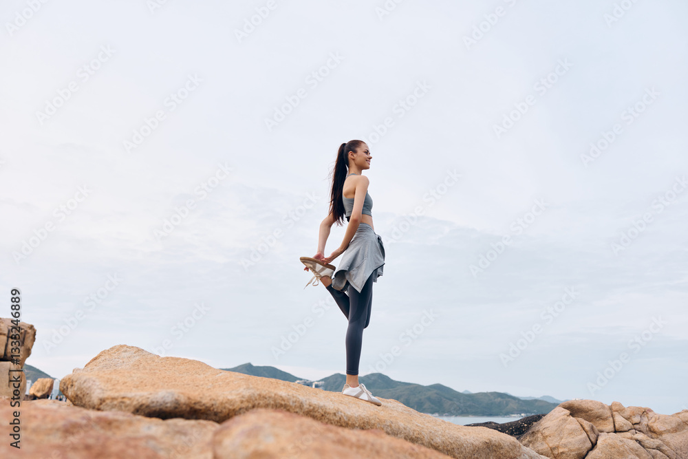 Naklejka premium Young woman practicing yoga on rocky terrain, showcasing strength and flexibility in sporty attire, embodying a healthy lifestyle and tranquility