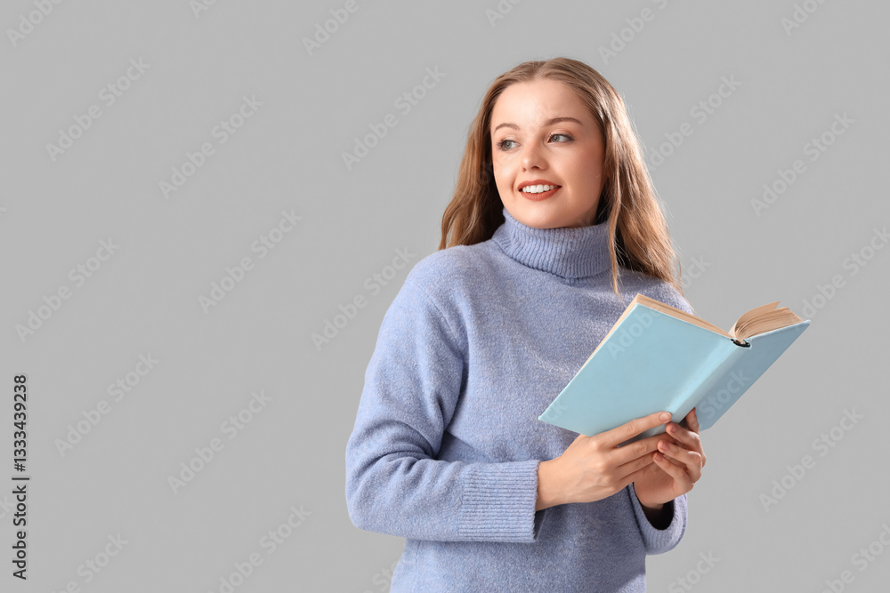 Happy beautiful young woman in warm sweater with book on grey background Happy beautiful young woman in warm sweater with book on grey background